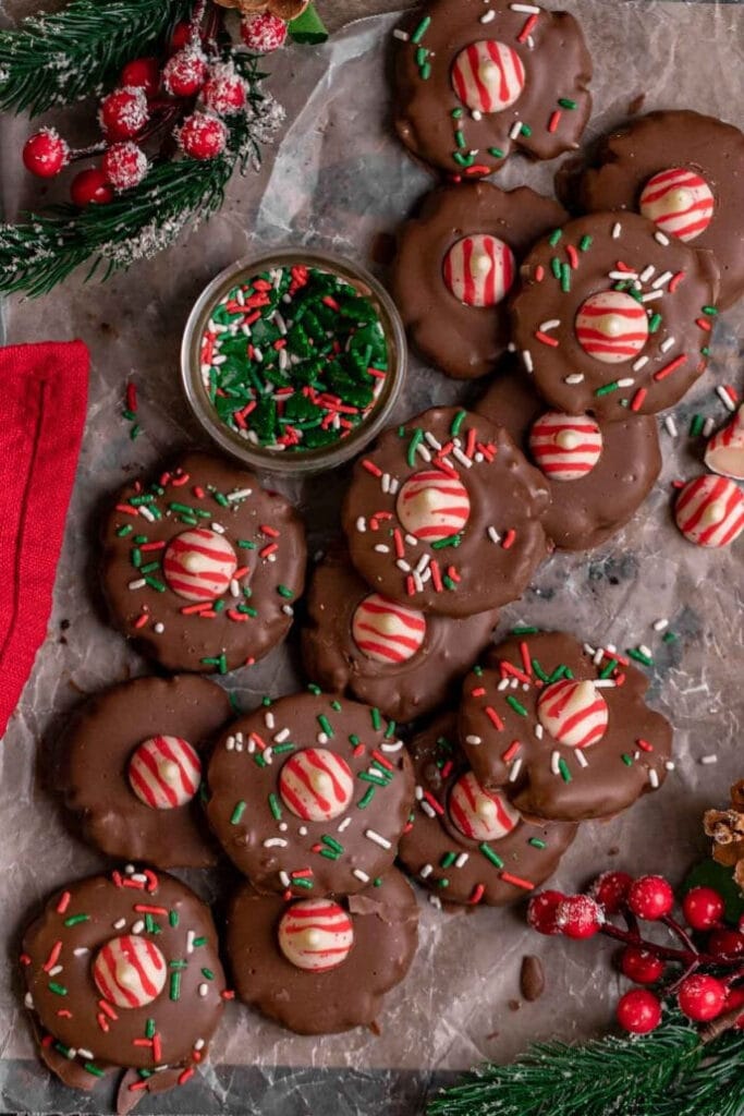 A dozen chocolate covered blossom cookies made with oreo crumbs and cream cheese, then decorate with hershey pepperment centers and Christmas sparkles.co sokies with hershey blossom peppermint centers decorating the top.
