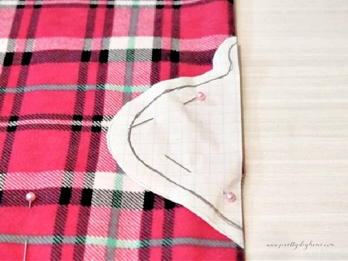 Paper pattern pinned to pink plaid flannel fabric for cutting out DIY Christmas ornaments.