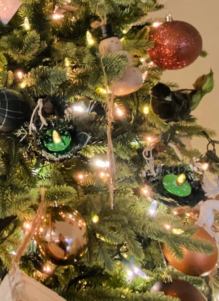 Glittered tart tin candle ornaments glowing on a Christmas tree with warm rustic lighting.