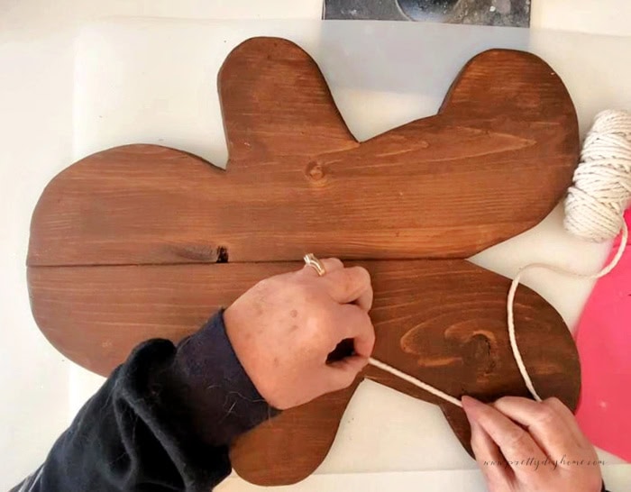 Applying macrame cord around the outside edge of a stained wooden gingerbread man to create a raised icing-style outline.