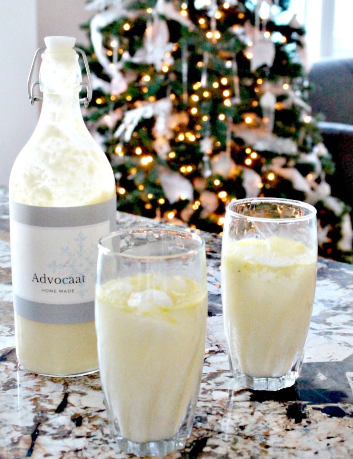 Bottle of homemade advocaat with two glasses of snowball cocktail on a festive table.