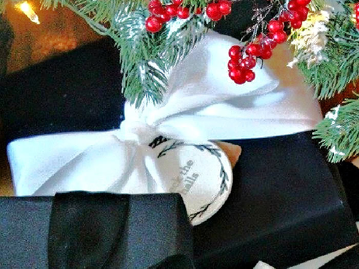 Close-up of black paper Christmas gift wrapping idea tied with white satin ribbon.