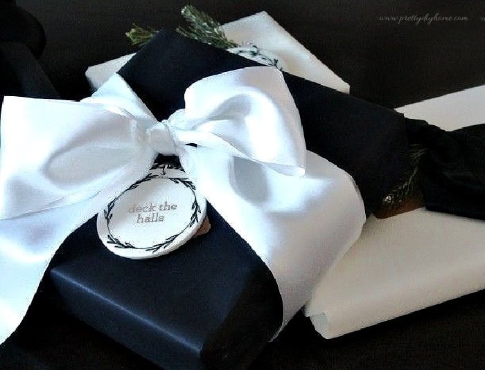 Close-up of black paper Christmas gift wrapping idea tied with white satin ribbon.