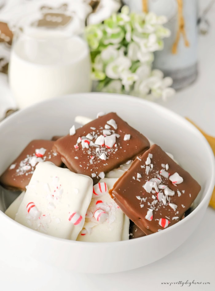 A white bowl of Christmas chocolate covered graham crackers beside a glass of milk and greenery.