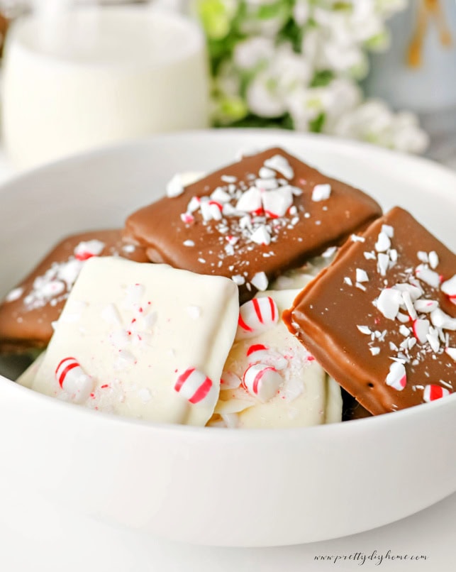 White bowl of Christmas chocolate covered graham crackers beside a glass of milk and greenery.