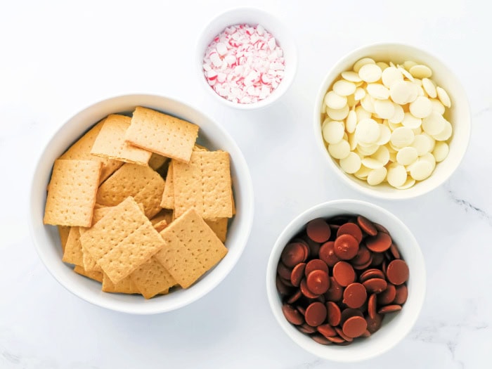 Ingredients for making Christmas chocolate covered graham crackers: graham crackers, white chocolate, milk chocolate, and crushed peppermint.