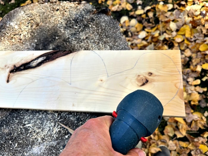 Cutting one half of a wooden gingerbread man shape from a 1x6 board using a jigsaw.