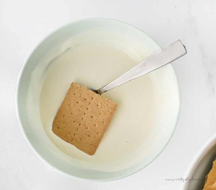 Hand dipping a graham cracker into melted white chocolate coating.