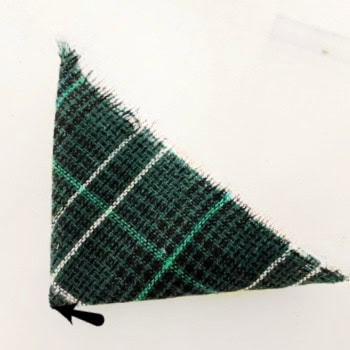 Folding tartan fabric to find the center before placing it inside a tart tin for a Christmas ornament, with an arrow to illustrate the center point.