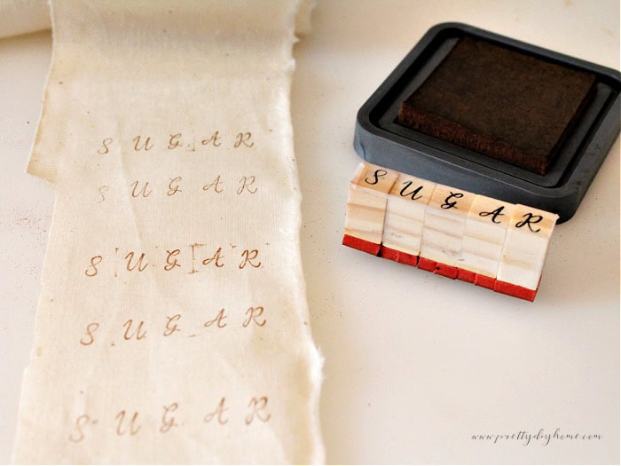 Hand stamping the word “Sugar” on a strip of muslin fabric to create labels for the white fabric gingerbread men.
