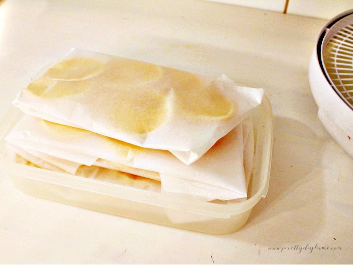Dried orange slices stacked in parchment paper bundles and stored inside a plastic container.