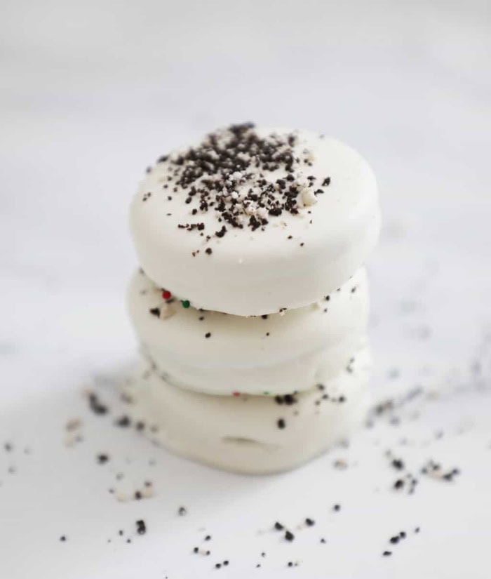 Three white fudge covered oreos with oreo crumb. They are stacked onto a white base and background.