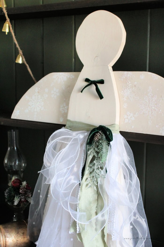 Finished wooden Christmas angel displayed on a dark green entryway cabinet, showing the muslin, pearl tulle, and green ribbon skirt with soft cottage core details,