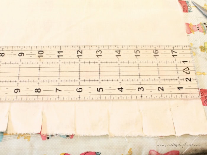 Measuring and snipping muslin with a ruler to prepare 1.5 inch fabric strips for the wooden Christmas angel’s skirt