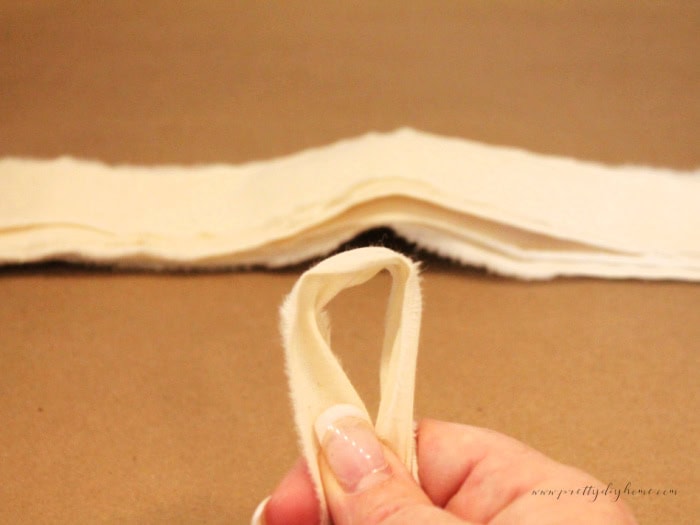 Close up showing how to hold a folded muslin strip to create the loop knot used to tie the skirt onto the wooden angel.