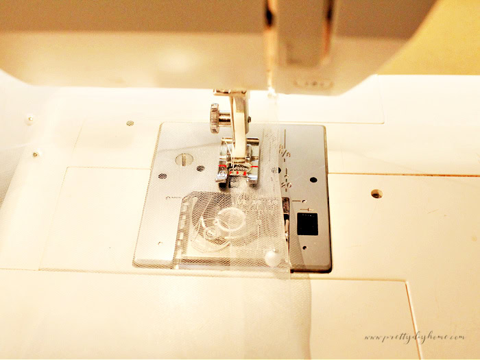 Sewing a zigzag stitch along the folded top edge of pearl tulle to create a drawstring overlay for the wooden angel’s skirt.