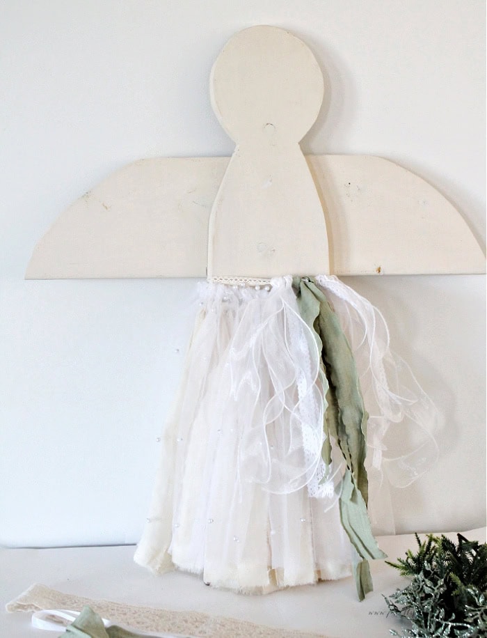 Wooden Christmas angel with all three skirt layers added, including muslin, pearl tulle, and staggered soft green and white ribbons.