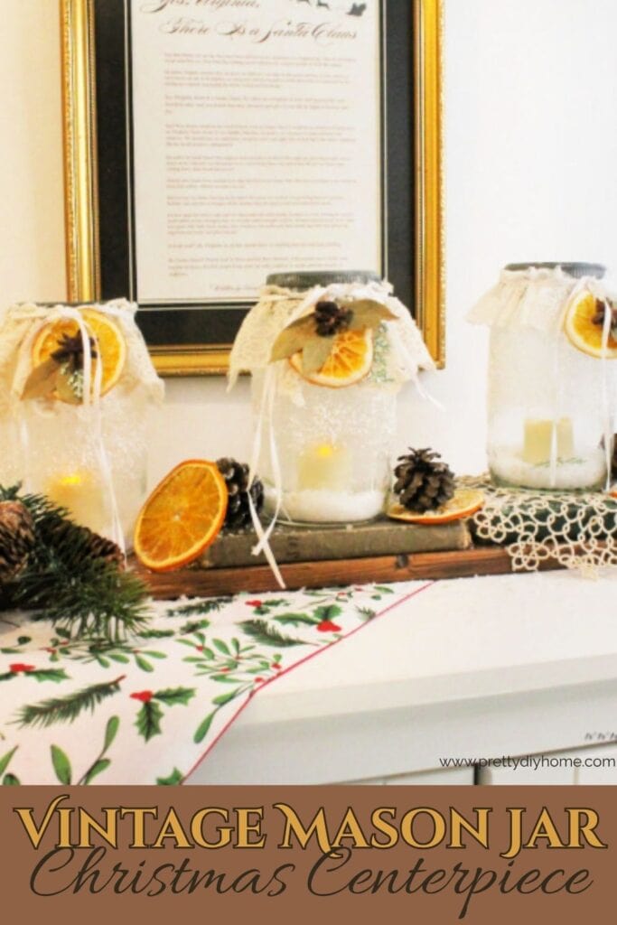 Vintage Christmas mason jar centerpiece with lace, frosted glass and dried oranges styled in front of a framed Yes Virginia printable