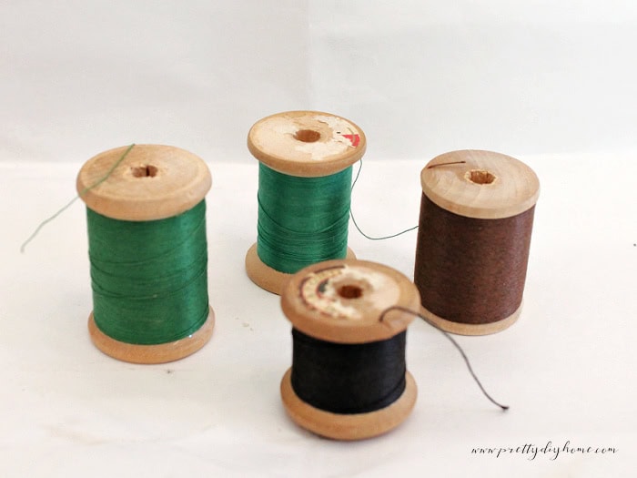 Four thrifted wooden thread spools before refinishing, showing aged surfaces and a mix of original thread colors.