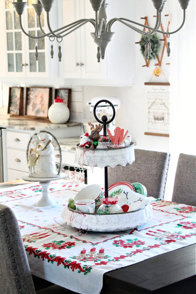 Christmas tiered tray centerpiece sitting on a vintage Christmas tablecloth in a small country kitchen.