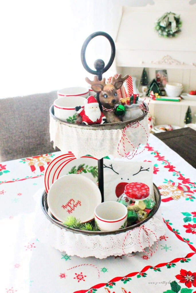 Completed vintage Christmas tiered tray centerpiece filled with holiday mugs, bowls, treats, and practical kitchen pieces.