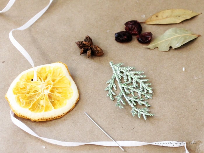 Supplies for making dried orange decorations including ribbon, anise pods, cranberries, and bay leaves