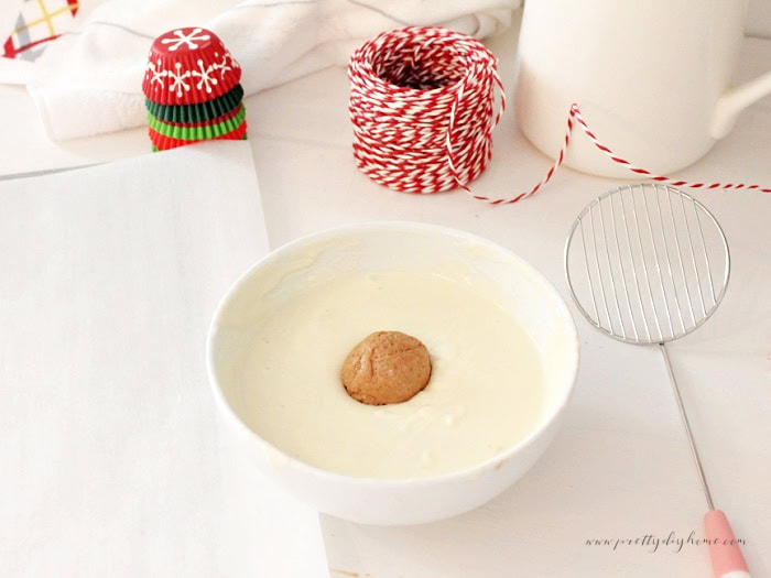 Dipping a gingerbread truffle into melted white chocolate for coating.