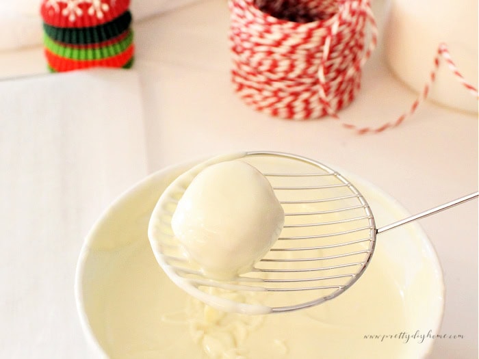 Lifting a coated gingerbread truffle from melted white chocolate with a candy sieve.
