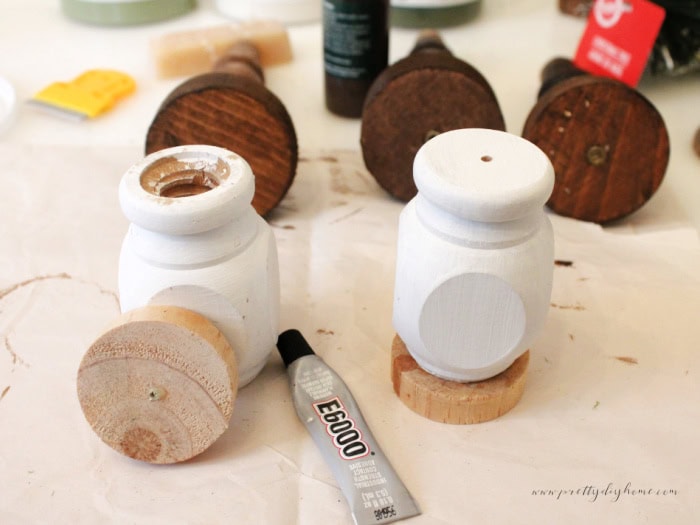 Two white spindles with wooden bases being glued on using E6000 for bottle brush tree stands.