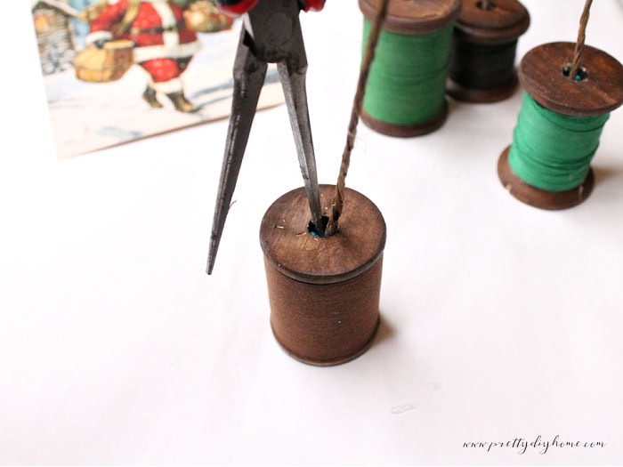 Using needle-nose pliers to push the puttied end of a paper-covered wire into the center hole of a stained wooden thread spool.