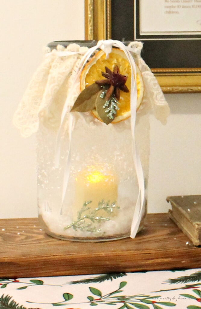 Dried orange slice used to decorate the front of a lace-wrapped jar with ribbon and greenery.
