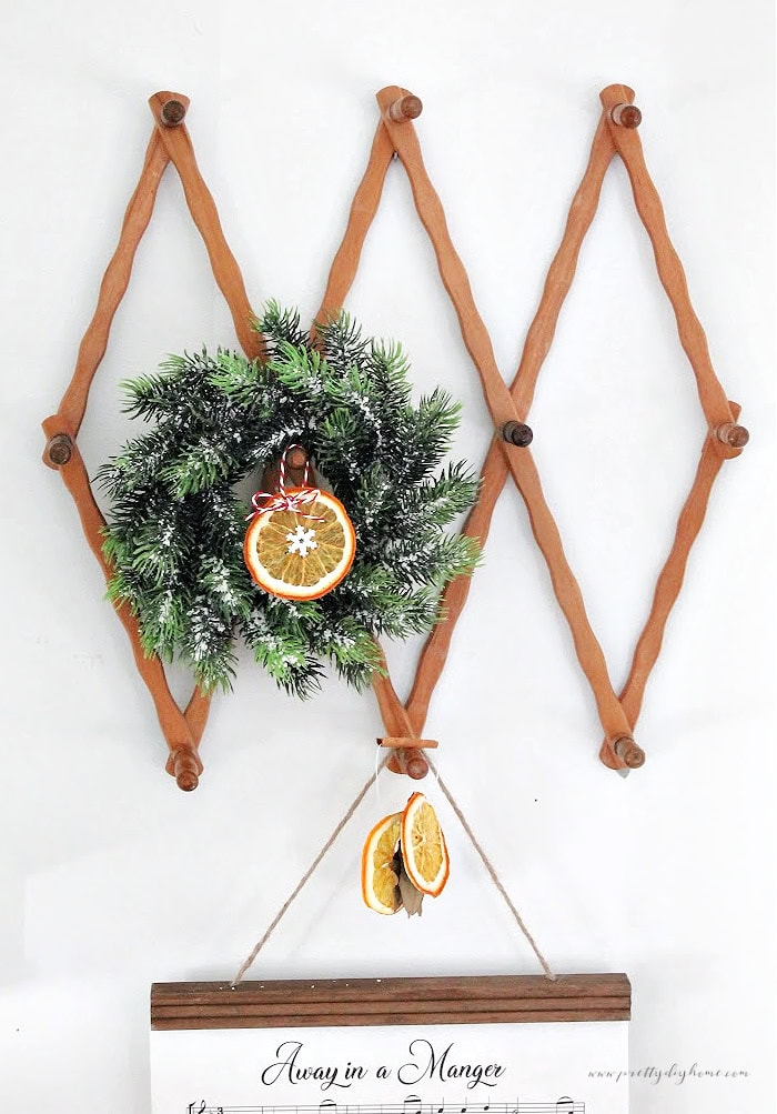 Dried orange slice ornament hanging from a small wreath displayed on a vintage wooden accordion rack.