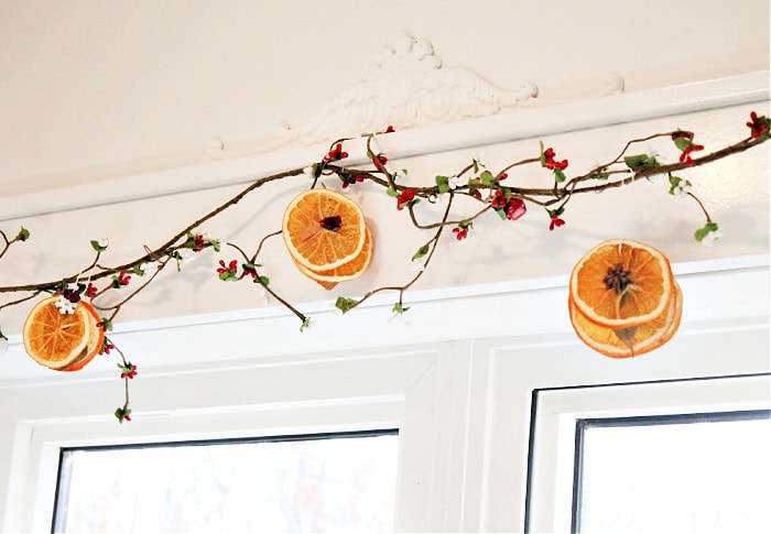 Three styles of dried orange slice ornaments hanging on a berry garland with white bells for natural Christmas décor.