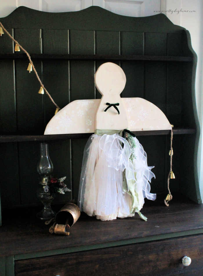 Cottage core wooden Christmas angel styled in a soft vintage Christmas vignette with muslin, pearl tulle, and green ribbon details.