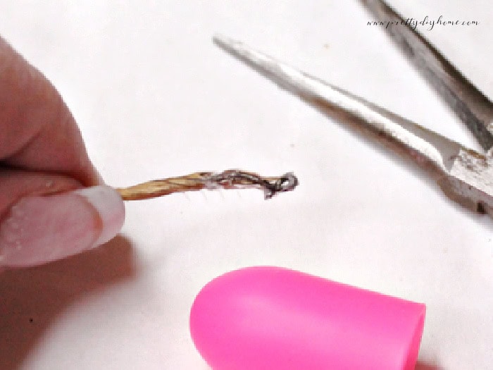 Beginning a wire photo holder by twisting the end backward into a small curl using needle-nose pliers.