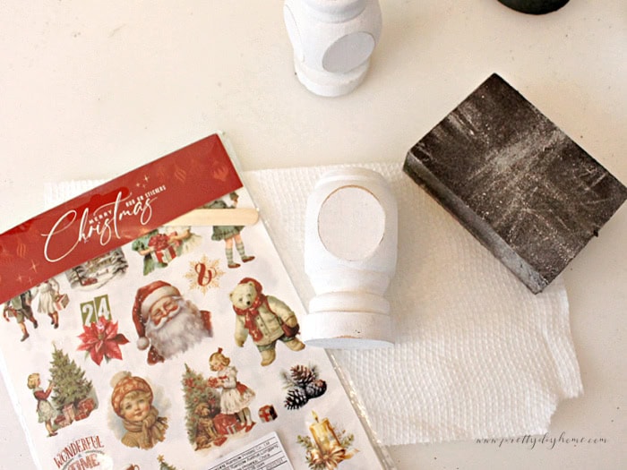 White spindle with distressed edges, sanding block, and rub-on Christmas transfers.