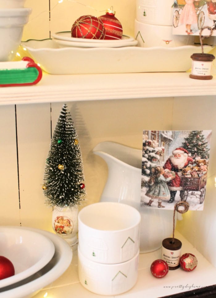 White spindle bottle brush tree displayed with vintage ironstone in a Christmas kitchen cupboard.