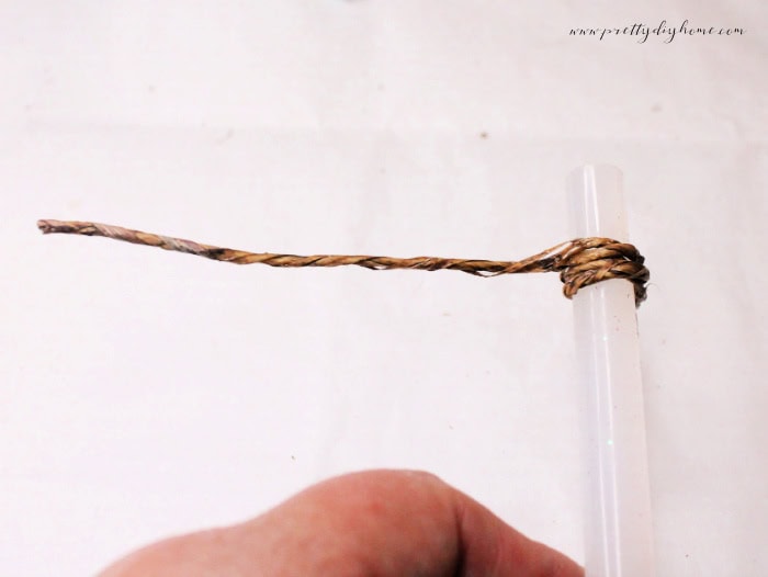 Close-up of paper-covered wire being wrapped around a glue stick to form smooth, even coils for a vintage postcard holder craft.