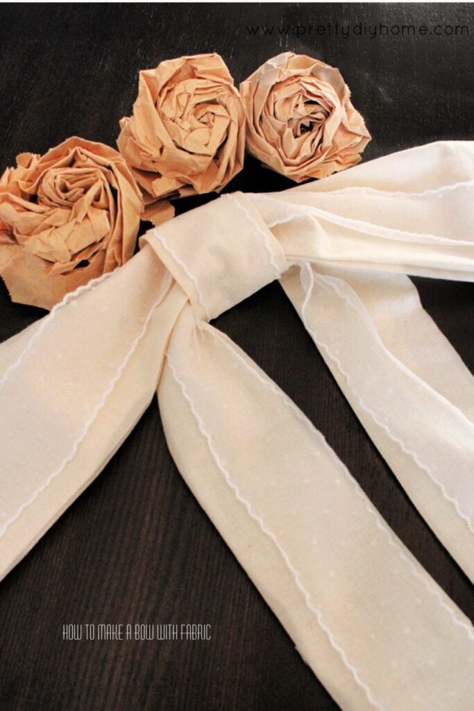 Handmade fabric bow with lace on a dark tabletop styled with paper bag roses