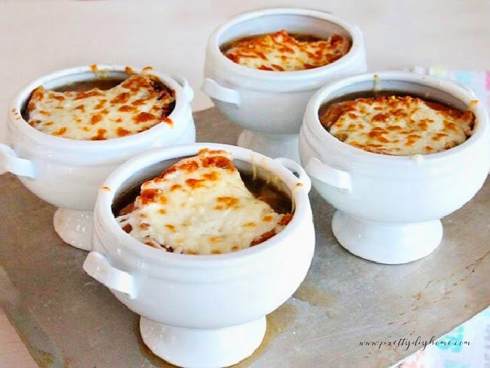 Four tureens of french onion soup just out of the oven with toasted garlic toast on top and metled cheese.