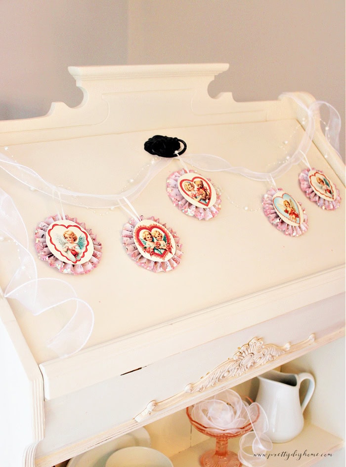 Vintage Valentine paper medallion banner with five cupid medallions displayed across a vintage secretary dresser