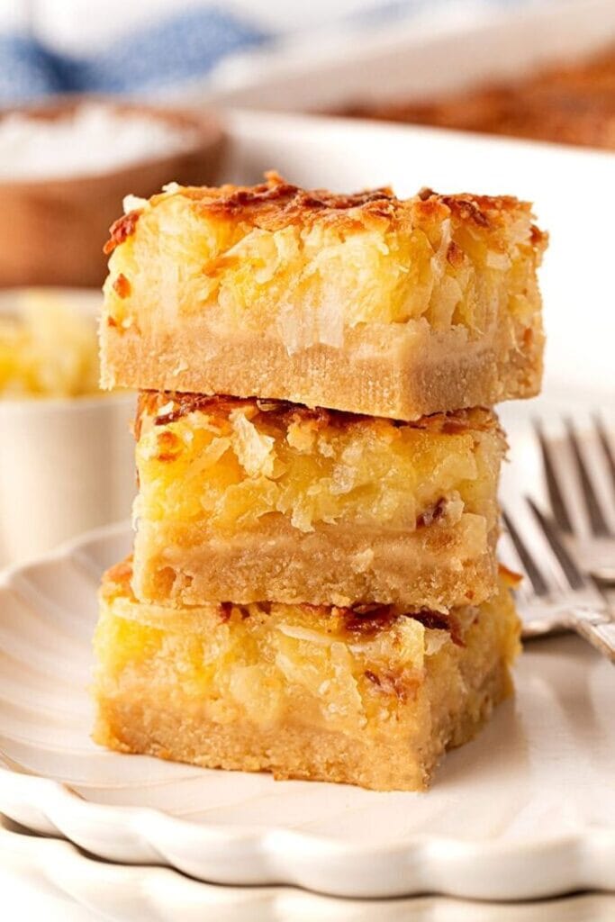 A stack of three Hawaiian dream bars showing the golden cookie crust on the bottom and the baked pineapple topping on top.