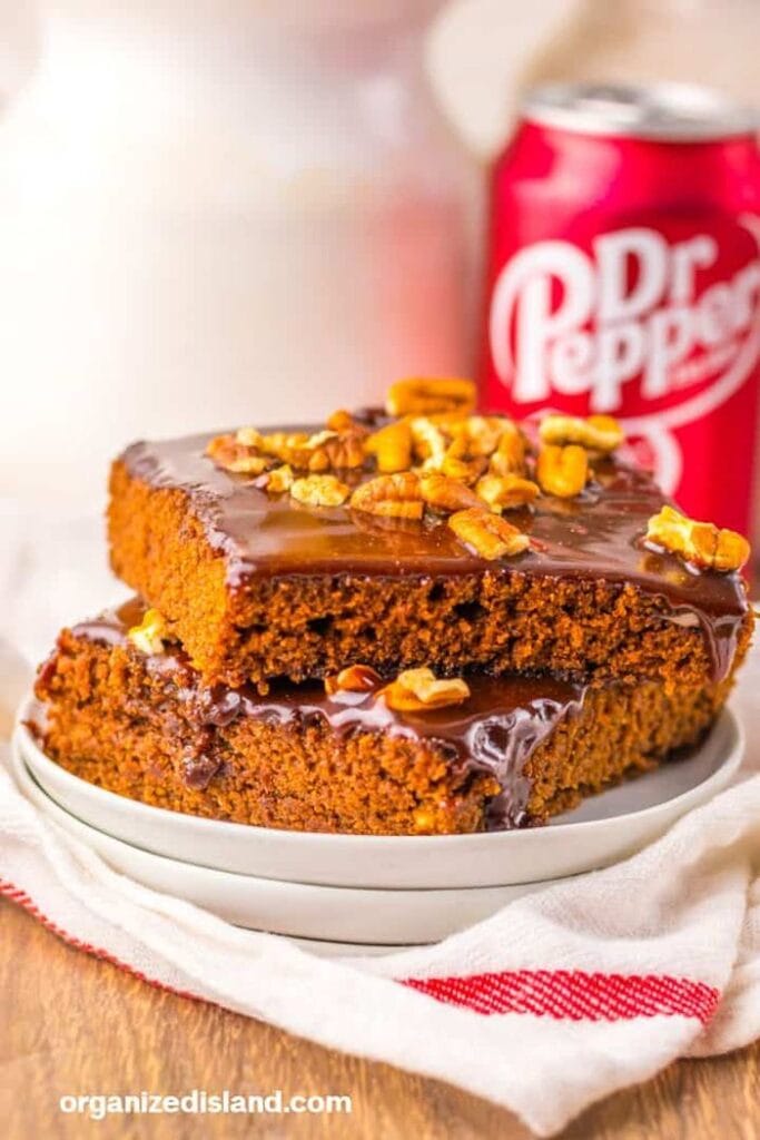 A stack of two slices of Dr Pepper cake topped with chocolate ganache frosting and walnuts.