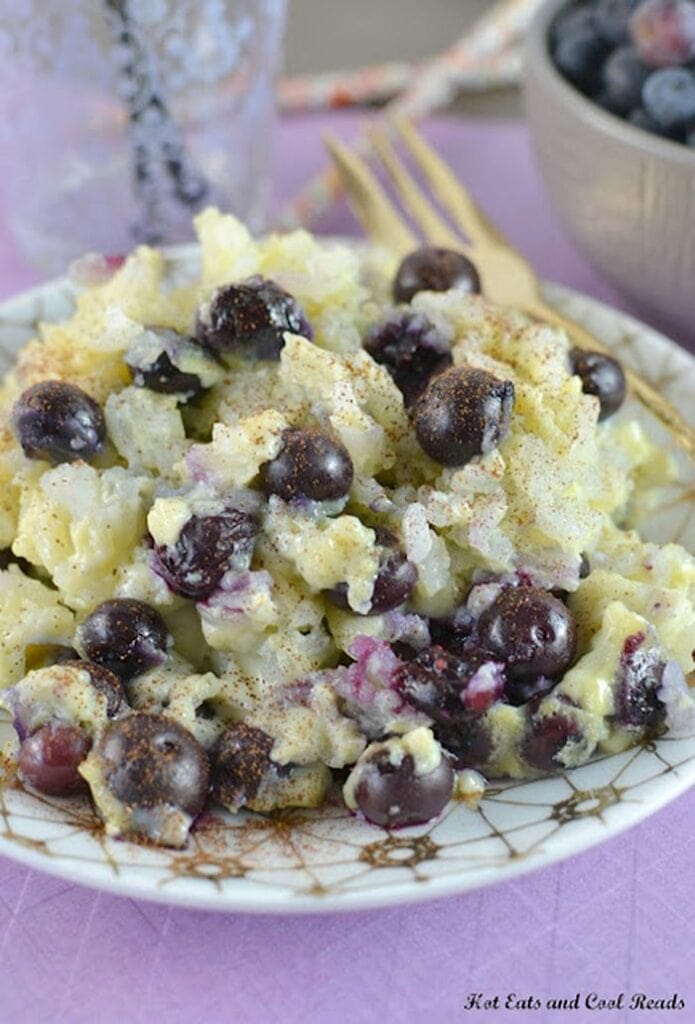 A gold and white plate filled to the brim with rice pudding mixed with plenty of juicy blueberries.