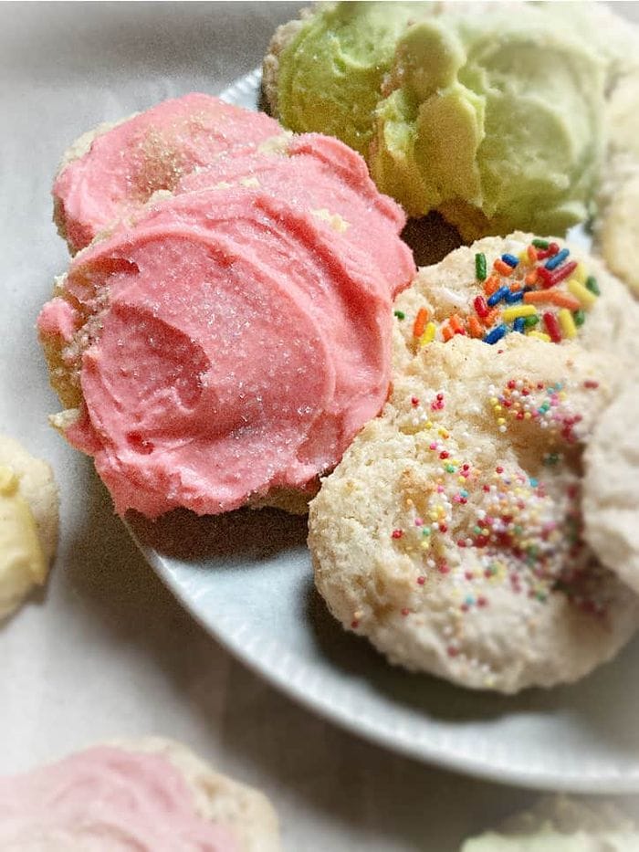 A tray of Granny’s sour cream cookies with three cookies shown on half of a plate, each topped with icing in green, pink, and white.