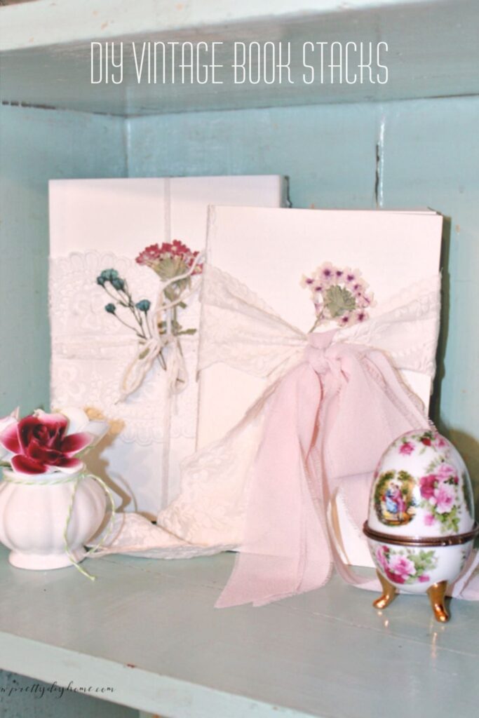 DIY decorative vintage book stacks wrapped in lace and ribbon with pressed dried flowers styled inside a vintage cabinet