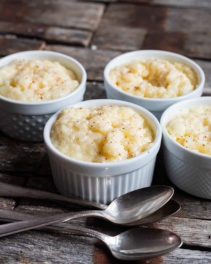 Four ramekins of classic tapioca pudding on a dark grey background with a spoon in front.
