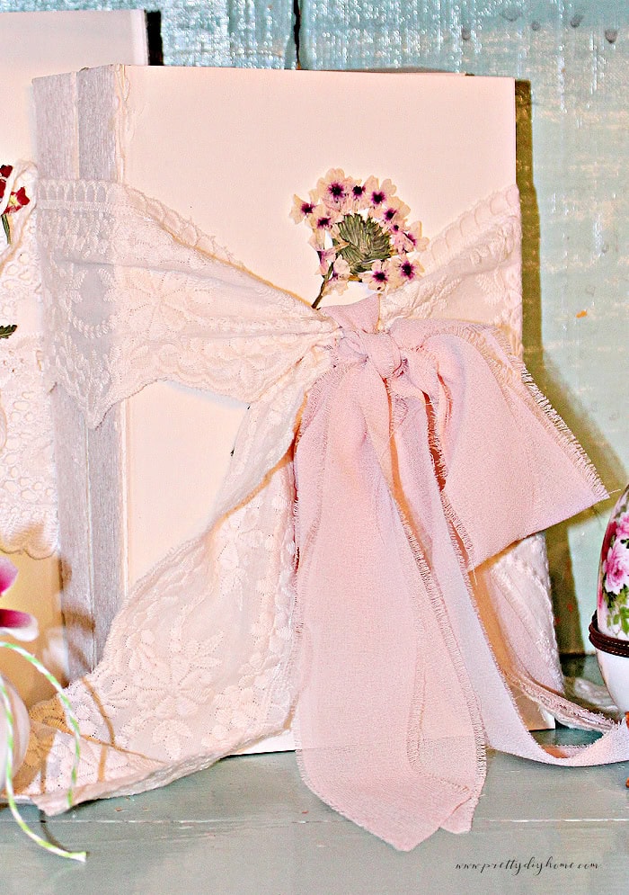 Muted pink ribbon tied over brocade ribbon on a decorative book stack