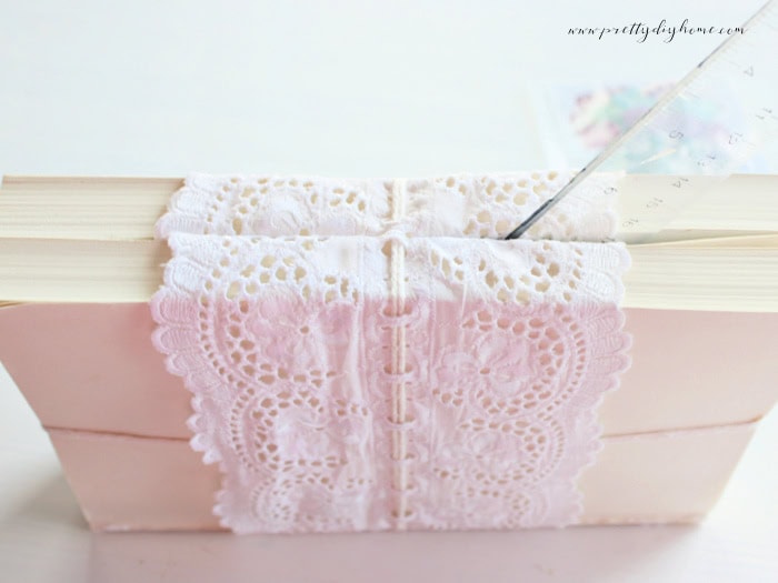 Using a ruler to tuck lace ribbon neatly between books in a decorative book stack