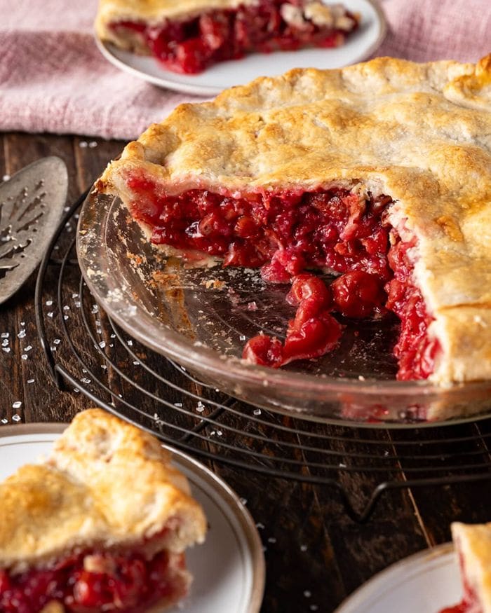 A large, luscious sour cherry pie with two slices cut out, shown with two pieces of pie arranged above and below the whole pie.